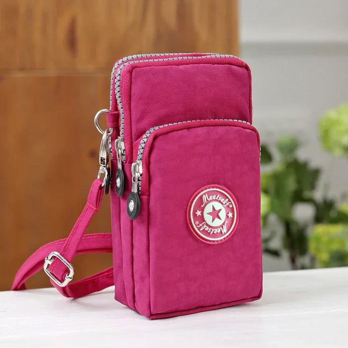 Compact pink crossbody bag with multiple zippered compartments and adjustable strap on white surface