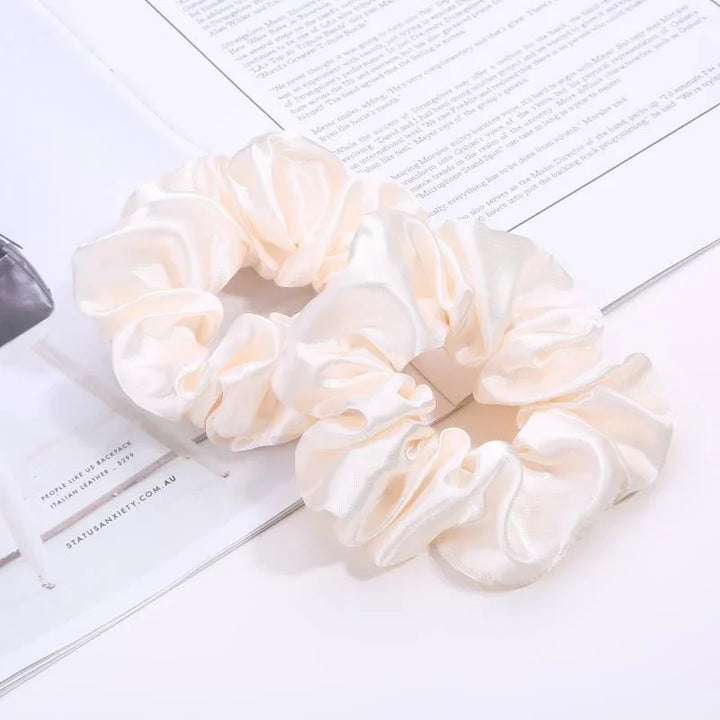 Two cream satin scrunchies lying on an open magazine page with text and minimalistic layout