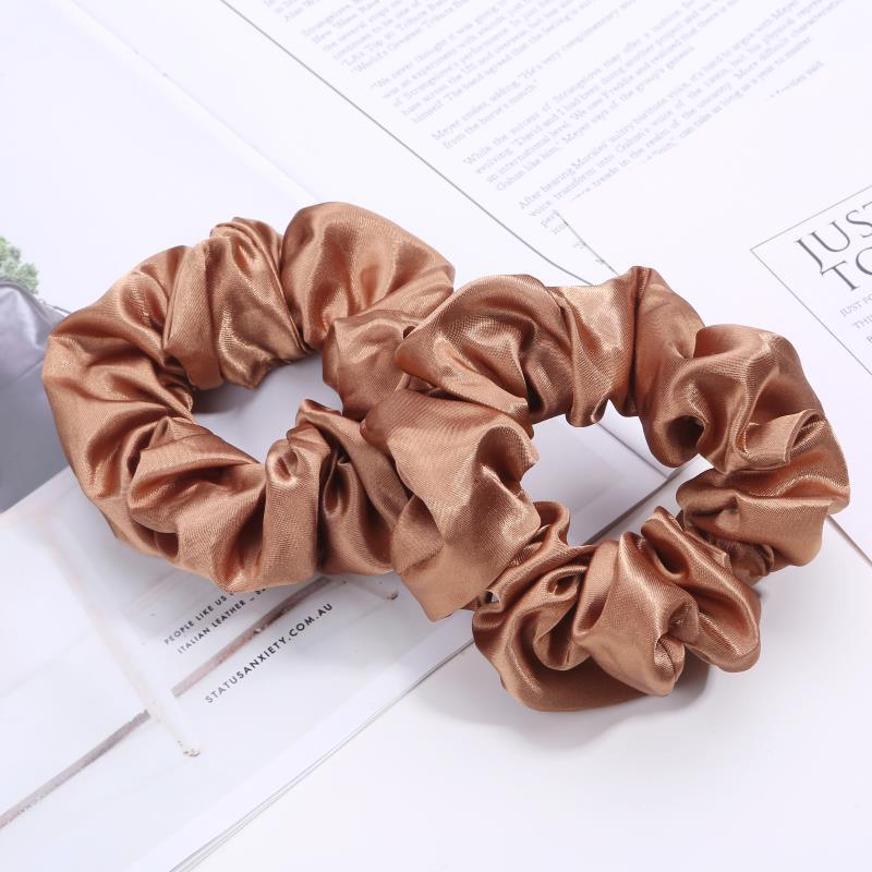Two shiny bronze satin hair scrunchies on white magazine pages background