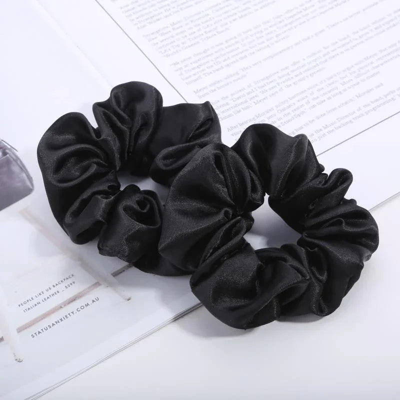 Two black satin hair scrunchies on an open magazine with white background