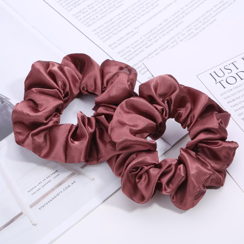 Two mauve satin scrunchies on white books and papers, soft fabric hair accessories