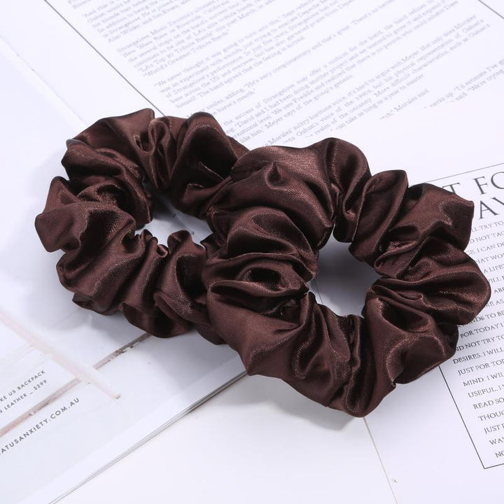Two dark brown satin scrunchies on an open magazine page