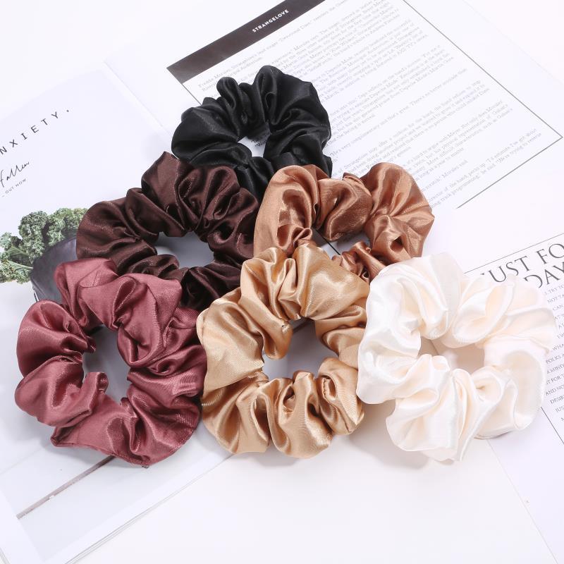 Set of six satin scrunchies in black, brown, bronze, beige, pink, and cream on printed paper background