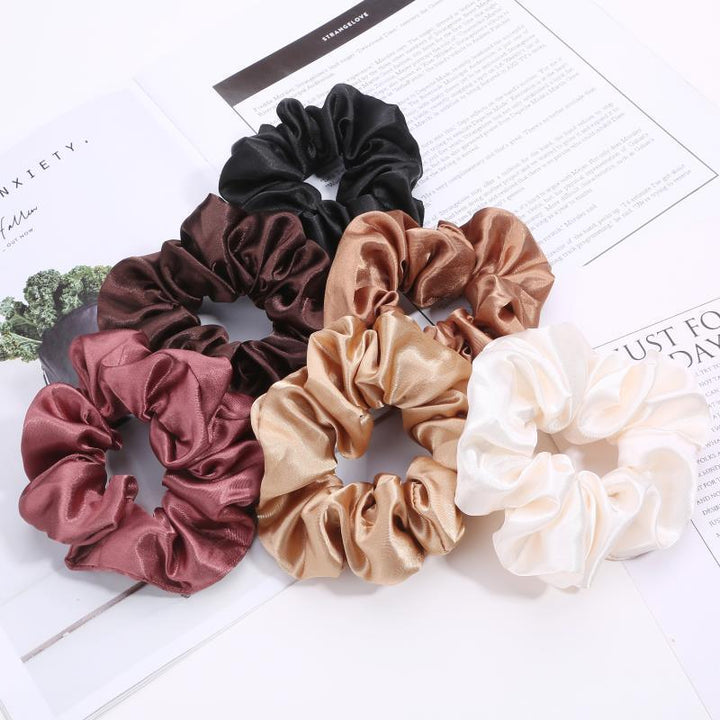 Set of six satin scrunchies in black, brown, bronze, beige, pink, and cream on printed paper background