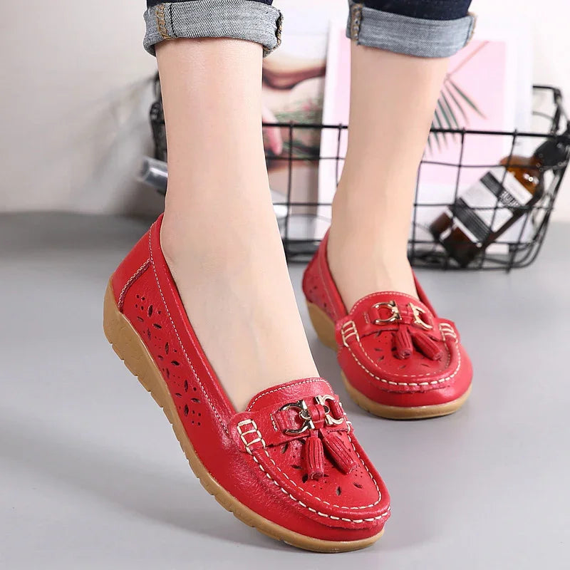 Red leather women's moccasins with tassels and perforated floral design, worn with cuffed jeans