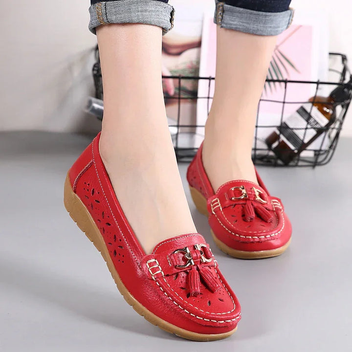 Red leather women's moccasins with tassels and perforated floral design, worn with cuffed jeans