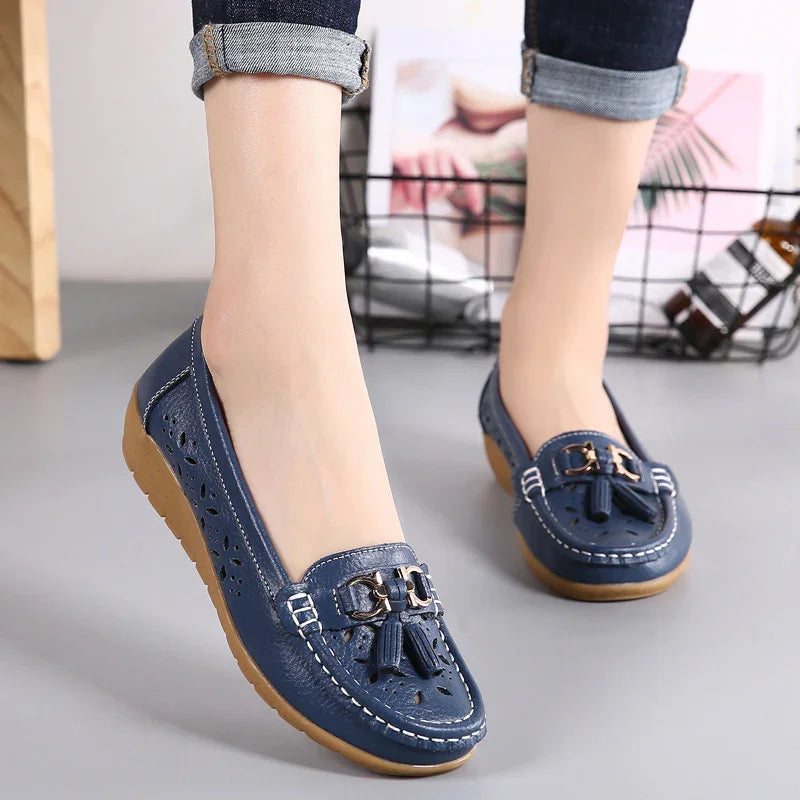 Blue leather loafers with tassels and perforated details worn with rolled-up jeans on gray floor