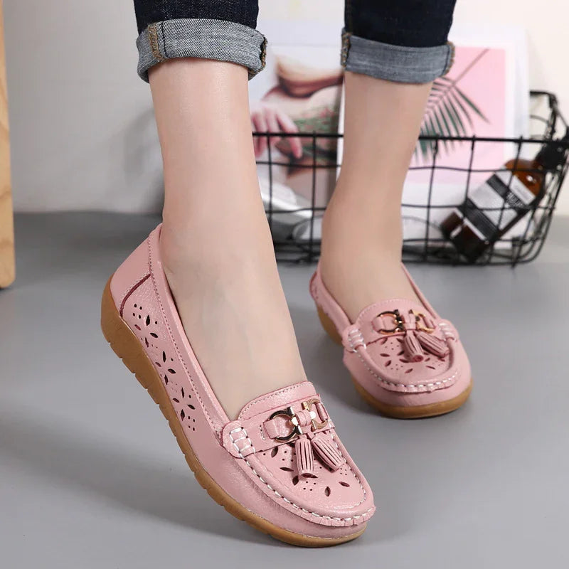 Close-up of pink leather loafers with tassel detail worn with rolled-up dark jeans on gray floor