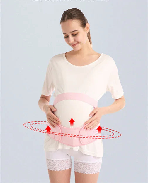 Pregnant woman wearing a pink maternity support belt over white clothes, gently holding her belly