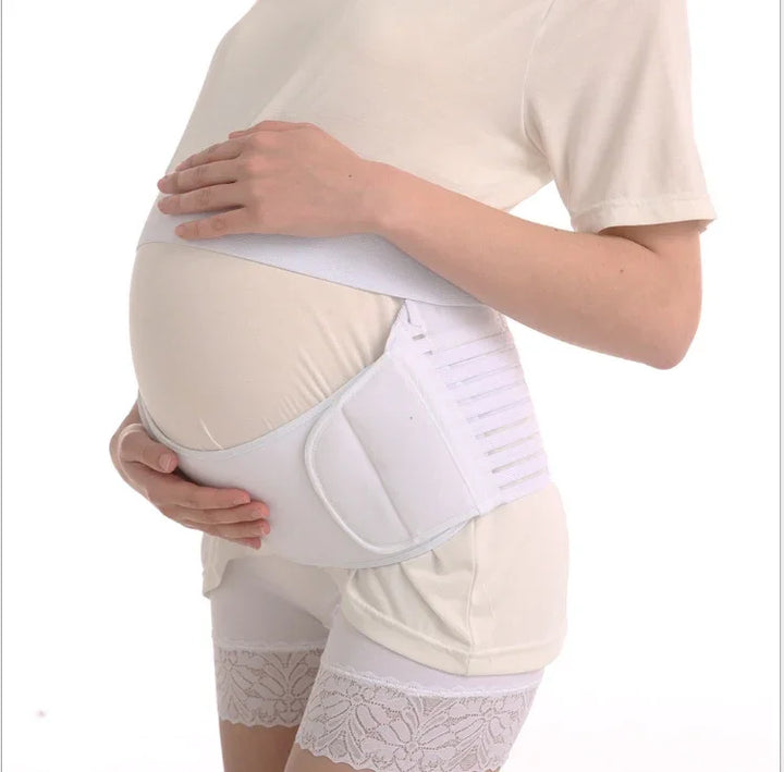 Pregnant woman wearing white maternity support belt and beige outfit, hands on belly