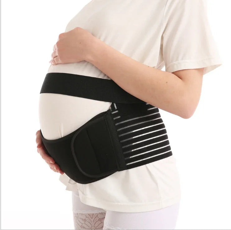 Pregnant woman wearing black adjustable maternity support belt over white shirt against white background