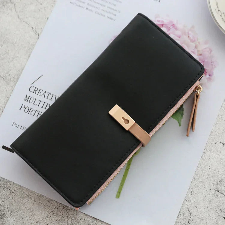 Black leather wallet with beige strap and gold lock detail on white magazine and pink flower