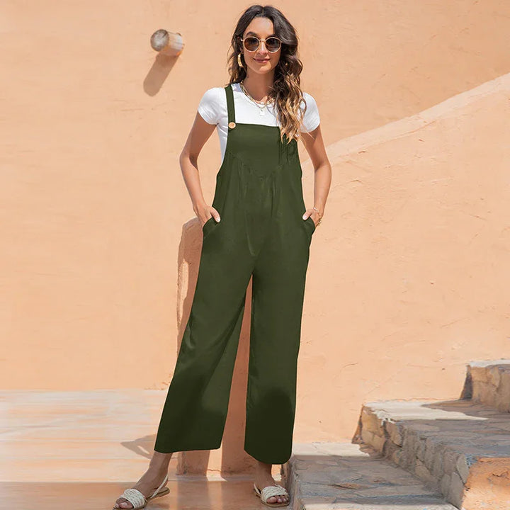 woman wearing olive green wide-leg overalls and white t-shirt standing by peach wall in stylish summer outfit