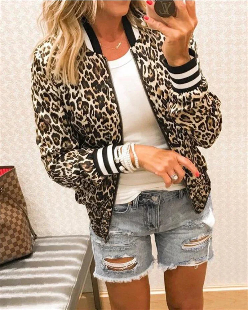 Woman wearing leopard print bomber jacket, white tank top, and distressed denim shorts taking mirror selfie
