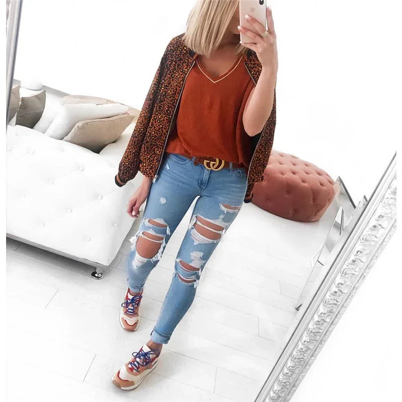 Woman taking mirror selfie wearing leopard print jacket, rust orange top, ripped skinny jeans, and sneakers