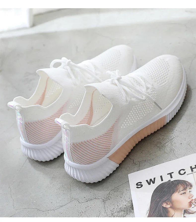 Pair of white lightweight knit sneakers with pink accents on a gray concrete floor next to a fashion magazine