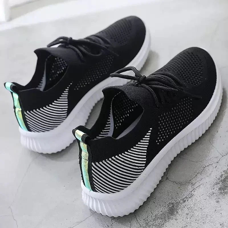 Black knit sneakers with white sole and reflective pull tab on concrete floor