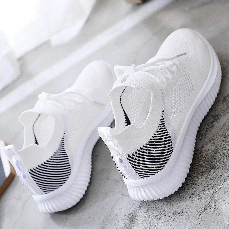 Pair of white knit sneakers with black striped heel detail and ribbed soles on gray floor