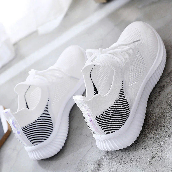 Pair of white knit sneakers with black striped heel detail and ribbed soles on gray floor