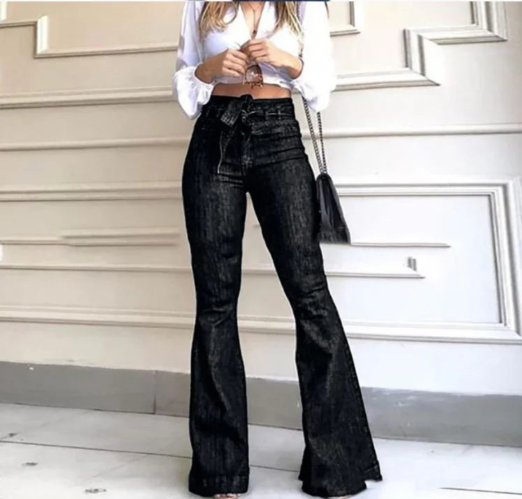 Woman wearing high-waisted black flare jeans and white cropped blouse standing against white paneled wall