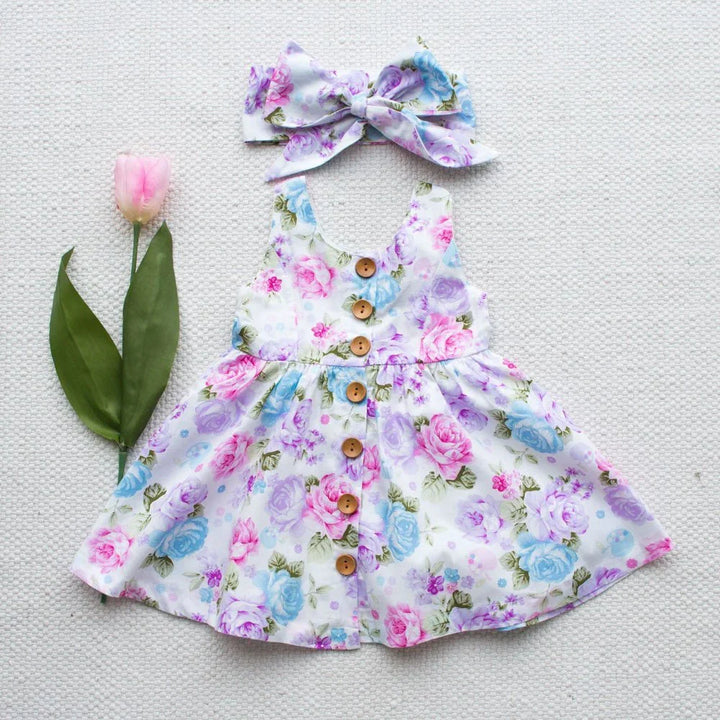 floral baby dress with wooden buttons and matching bow headband on textured white background with pink tulip
