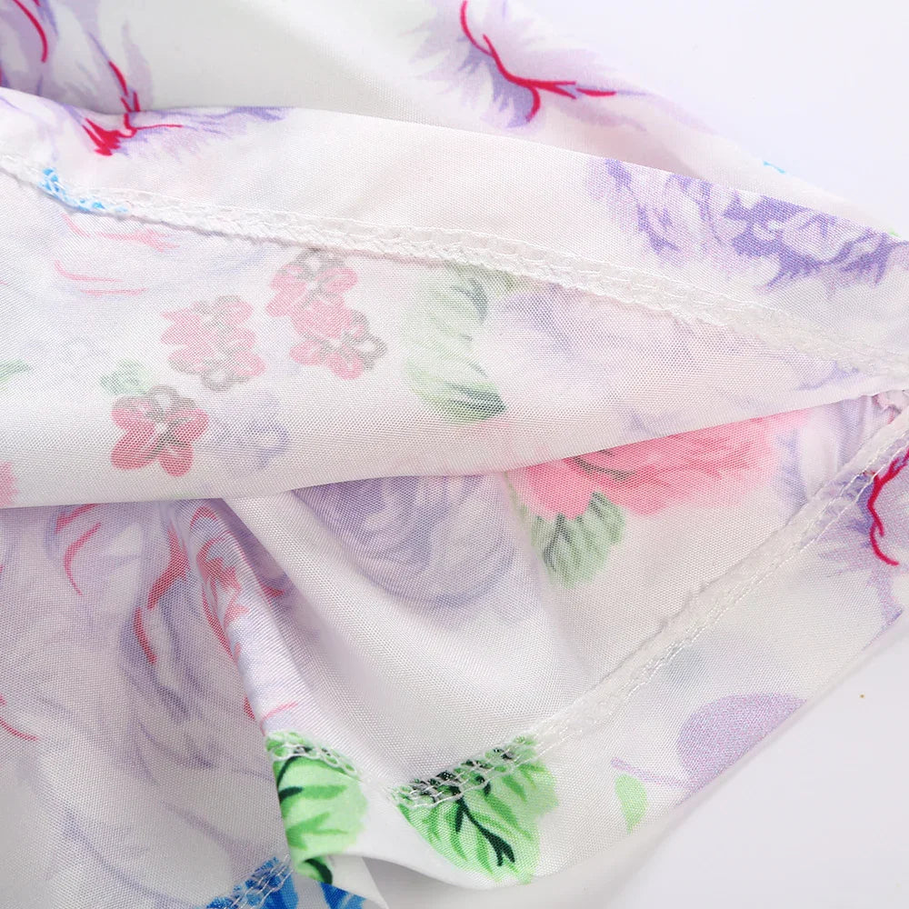Close-up of white floral patterned fabric with pink, purple, and green flowers and detailed stitching