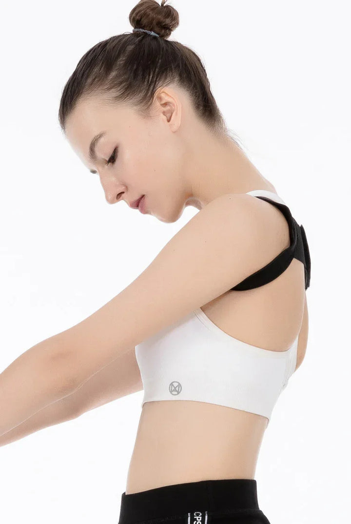 Young woman wearing white sports bra with black straps and black workout pants, posing side profile