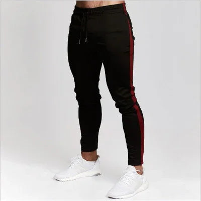 Men's black jogger pants with red side stripes and white sneakers on plain background