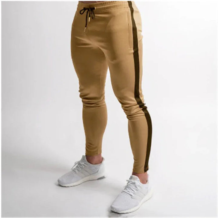 Men's beige jogger pants with black side stripes and white athletic sneakers on a white background