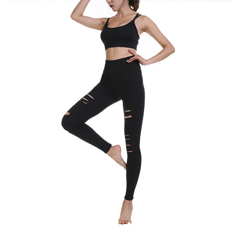 Woman wearing black ripped leggings and a black sports bra in a yoga pose on white background