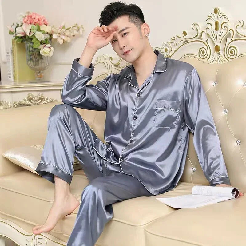 Man wearing shiny gray silk pajamas sitting barefoot on ornate cream sofa with floral decor and open magazine