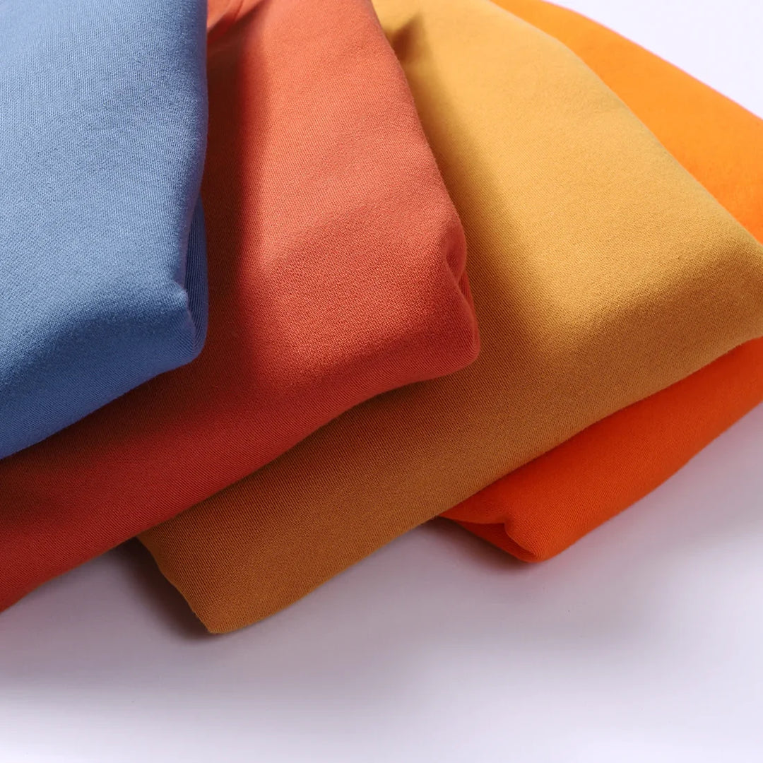 Stack of folded fabric in blue, rust, mustard, and orange colors on a white background