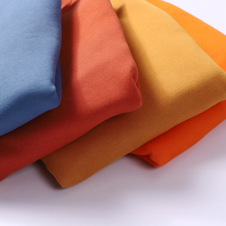 Stack of folded fabric in blue, rust, mustard, and orange colors on a white background