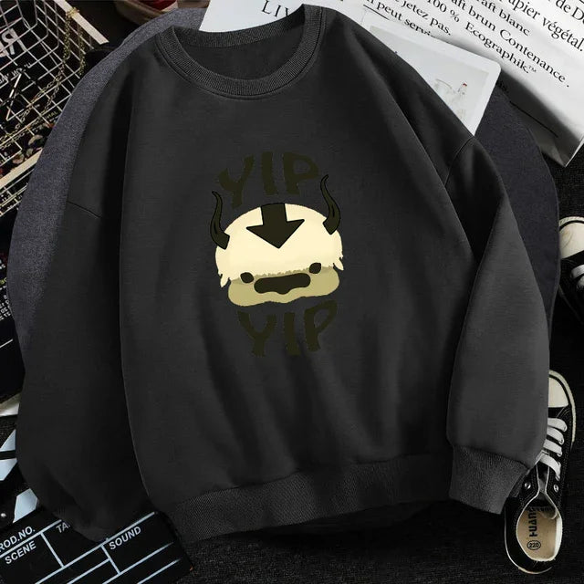 Black sweatshirt with cartoon Appa face and 'Yip Yip' text from Avatar series, laid flat with sneakers