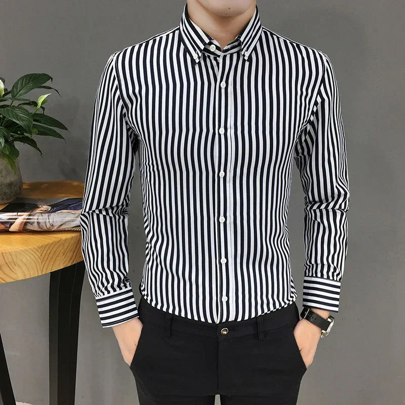 Man wearing a black and white vertical striped button-up shirt with black pants, standing indoors