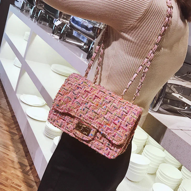 Woman wearing beige sweater and black skirt holding a pink woven chain strap handbag indoors