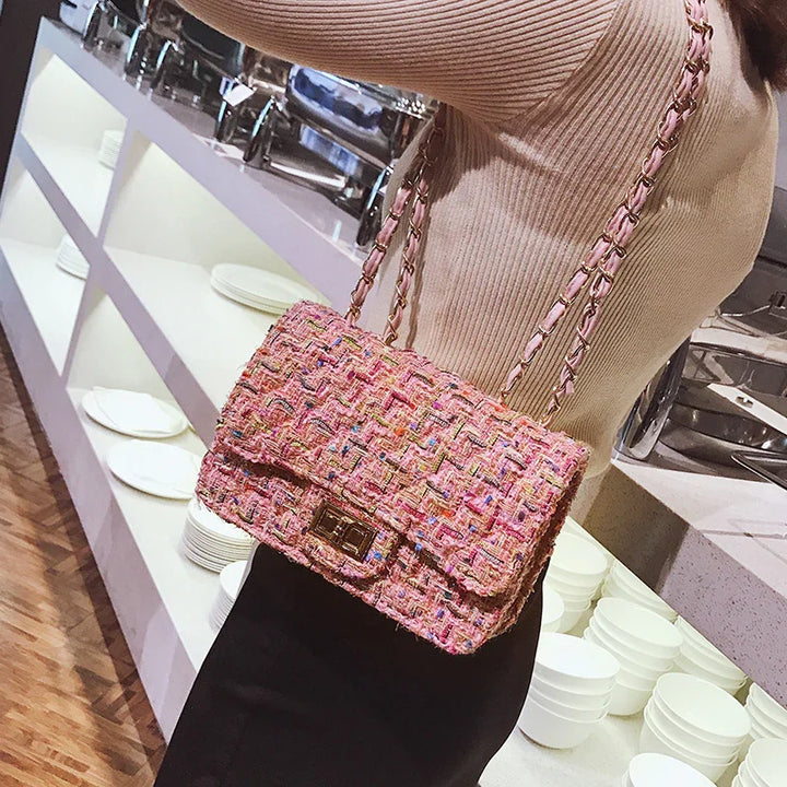 Woman wearing beige sweater and black skirt holding a pink woven chain strap handbag indoors