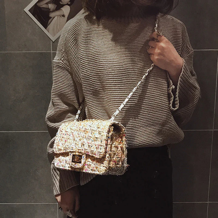 Person wearing brown knit sweater holding a beige tweed handbag with chain strap in indoor setting