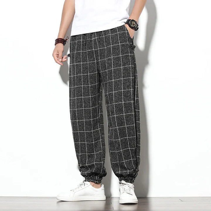 Men's casual black and white checkered jogger pants with elastic cuffs, paired with white sneakers