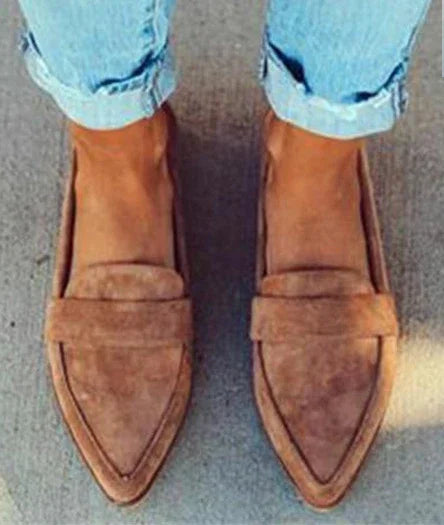 Person wearing light blue rolled jeans and brown suede pointed loafers on concrete floor