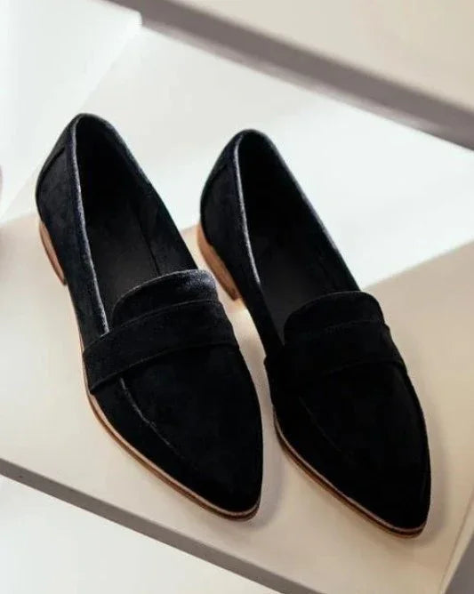 Pair of black suede pointed-toe loafers with tan soles displayed on a white surface
