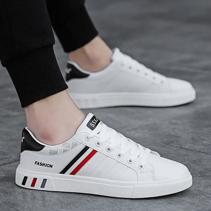 White low-top fashion sneakers with black and red stripes worn with black pants on gray pavement
