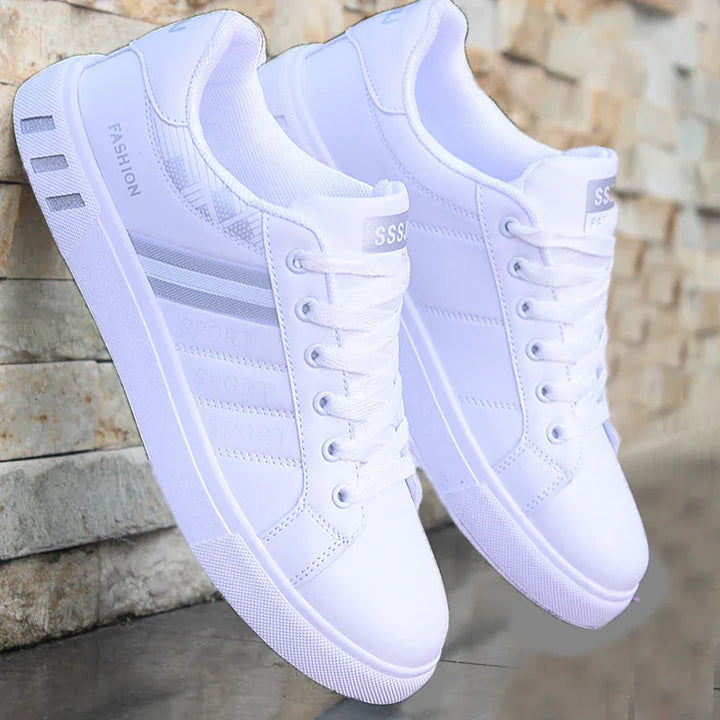 Pair of white casual sport sneakers with lace-up design and striped accents against stone wall