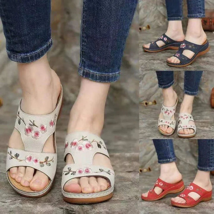 women's floral embroidered slip-on sandals in beige, red, and navy blue with wooden soles worn with blue jeans