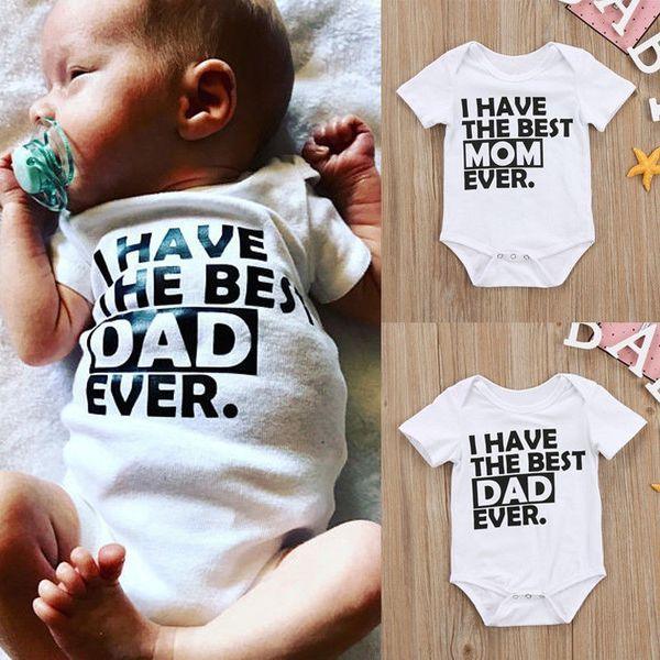 Baby wearing white onesie with black text I HAVE THE BEST DAD EVER, plus white onesies with Mom and Dad text on wooden background