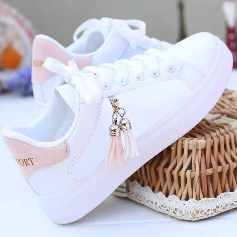 white sneakers with pink heel tab and decorative tassels on white sole against wicker basket
