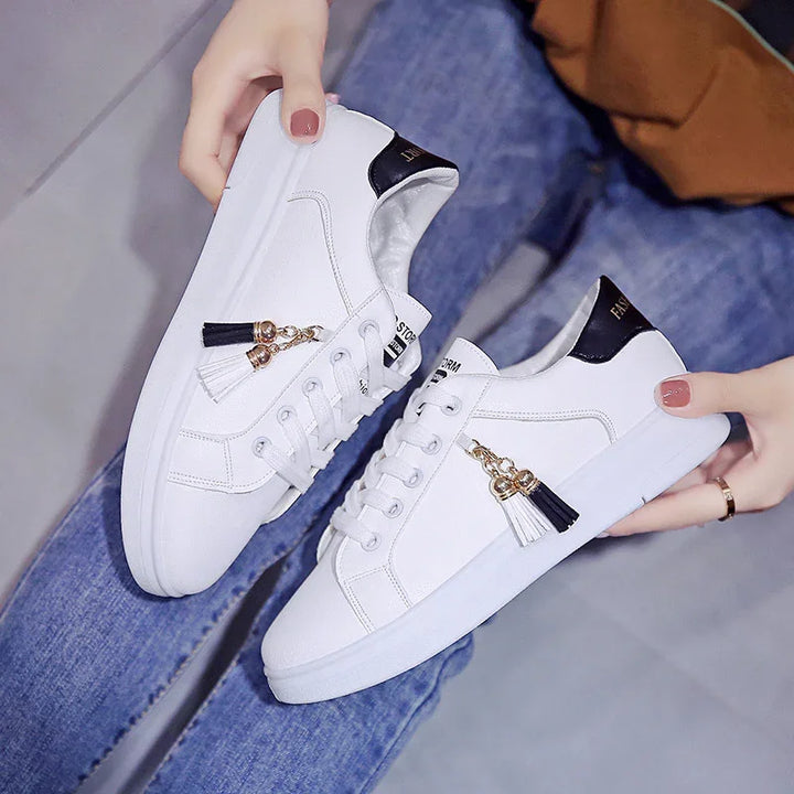 White casual sneakers with black and white tassel charms and black heel detail held by person in blue jeans