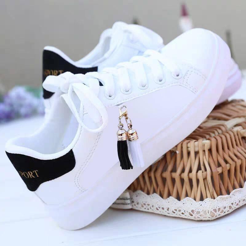 White casual sneakers with black heel detail and black and white tassel charm on wicker basket