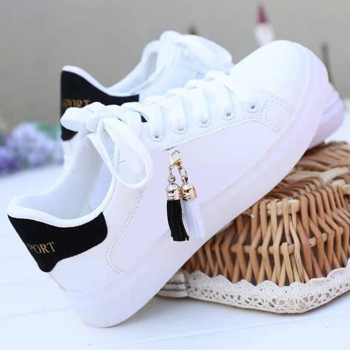 White casual sneakers with black heel detail and black and white tassel charm on wicker basket