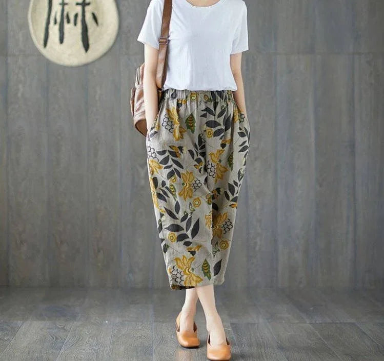 Woman in white t-shirt and floral patterned loose pants with pockets, wearing tan heels, brown bag